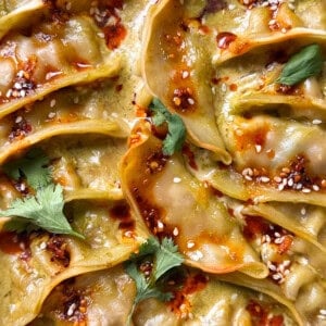A close-up of several dumplings from a viral Dumpling Bake, topped with chili oil, sesame seeds, and cilantro leaves, arranged in a visually appealing pattern.