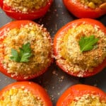 Six stuffed tomatoes, made with our classic stuffed tomatoes recipe and filled with a golden crumb mixture, are garnished with fresh parsley and arranged close together on a dark surface.