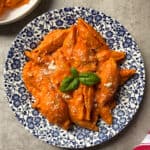 Pasta shells covered in creamy tomato sauce, garnished with grated cheese and fresh basil, served on a blue and white floral plate on a gray surface—an inviting unstuffed shells recipe perfect for any occasion.