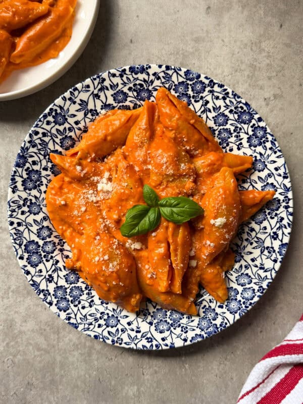 Pasta shells covered in creamy tomato sauce, garnished with grated cheese and fresh basil, served on a blue and white floral plate on a gray surface—an inviting unstuffed shells recipe perfect for any occasion.