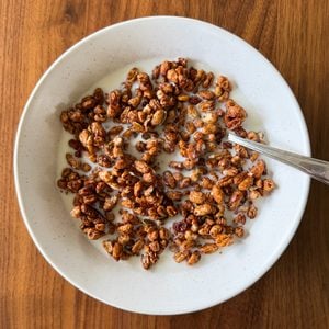 A white bowl of chocolate breakfast cereal made from a delicious homemade cereal recipe with milk and a spoon sits on a wooden table.