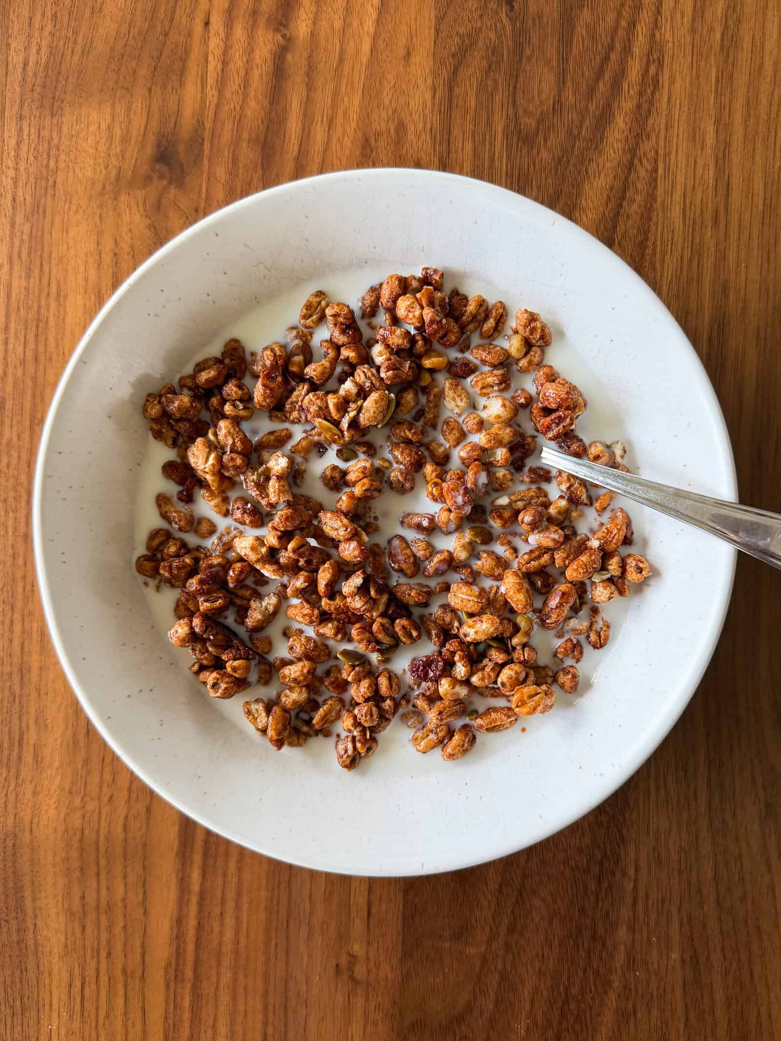 A white bowl of chocolate breakfast cereal made from a delicious homemade cereal recipe with milk and a spoon sits on a wooden table.