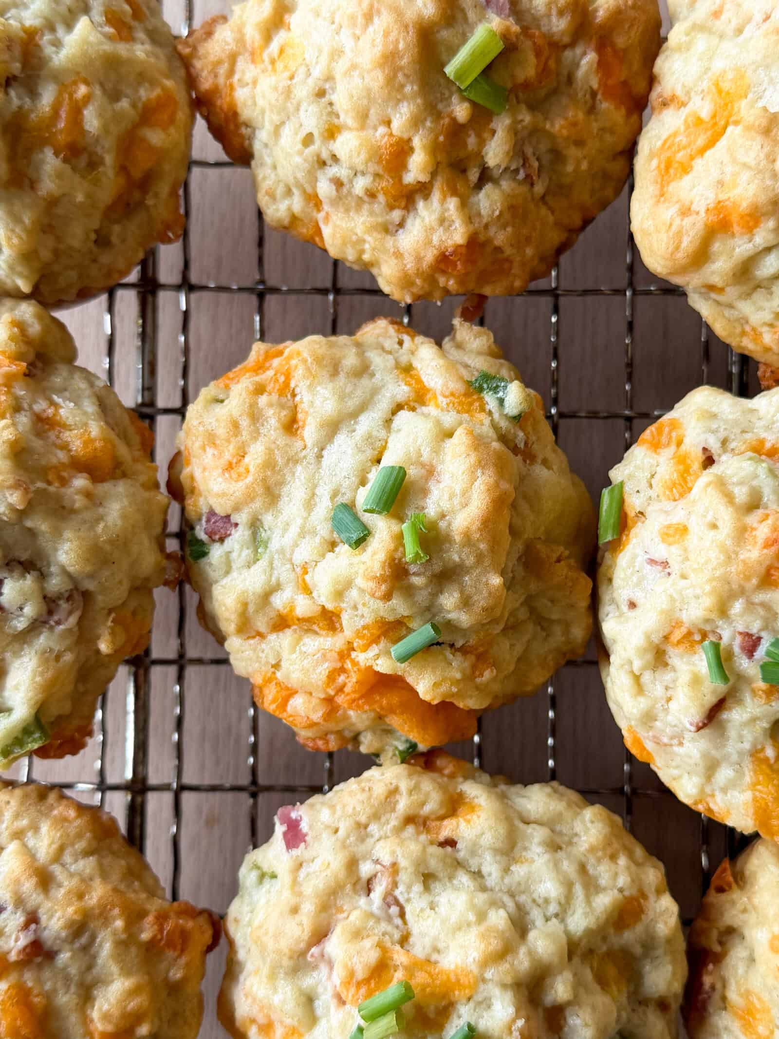 Close-up of savory breakfast muffins with cheddar cheese, bacon, and chopped green onions, cooling on a wire rack. This irresistible breakfast muffins recipe offers the perfect balance of flavors for a delicious morning treat.