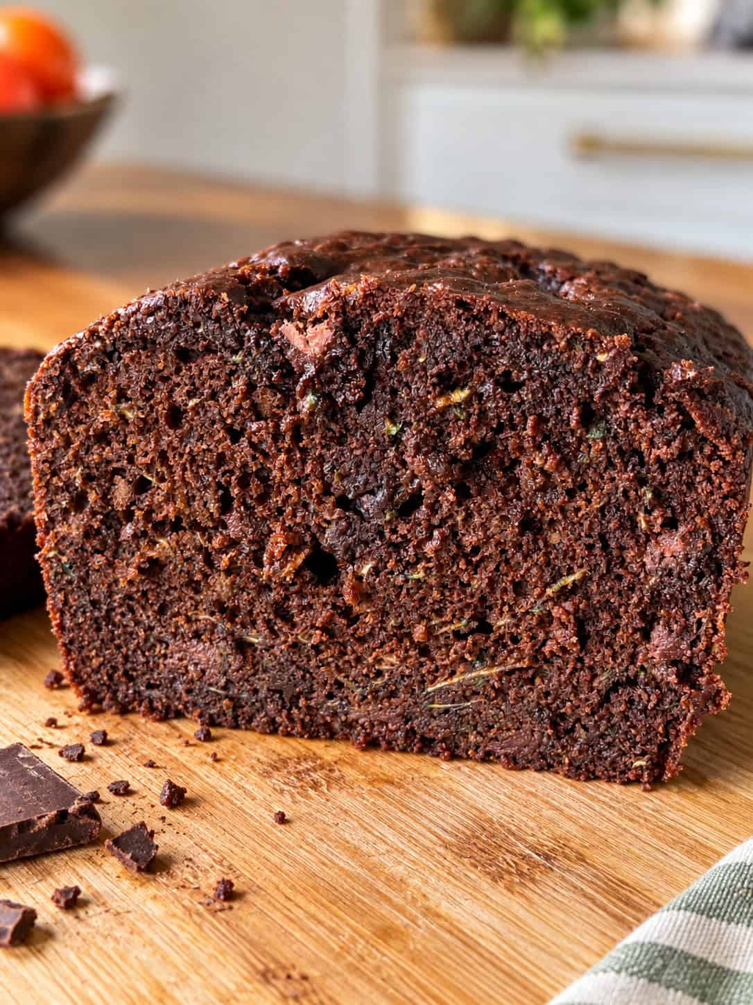 A close-up of a sliced loaf of moist Chocolate Zucchini Bread on a wooden cutting board, with chocolate pieces nearby and a blurred kitchen background, perfectly capturing the rich texture and appeal of this delightful Chocolate Zucchini Bread recipe.