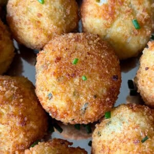 Golden-brown, crispy fried mashed potato balls garnished with small bits of chopped chives, arranged closely together on a metal tray&mdash;these delicious bites are the perfect answer to what to do with leftover mashed potatoes.