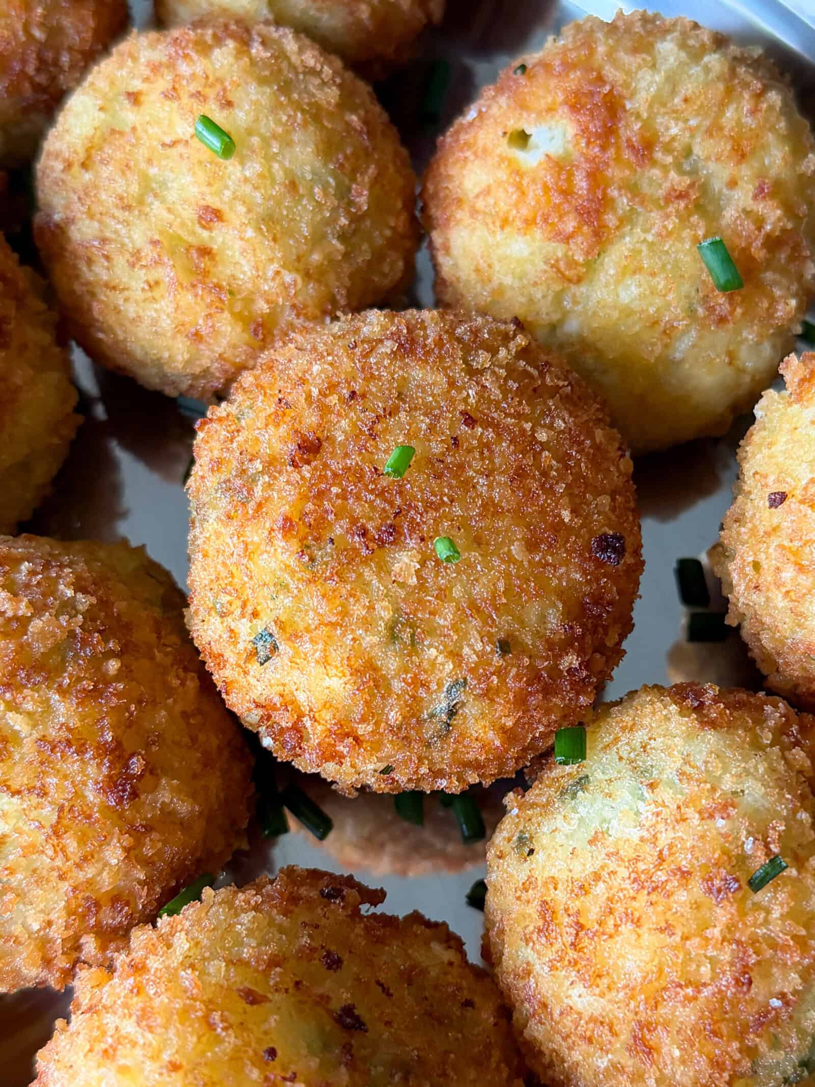 Golden-brown, crispy fried mashed potato balls garnished with small bits of chopped chives, arranged closely together on a metal tray&mdash;these delicious bites are the perfect answer to what to do with leftover mashed potatoes.