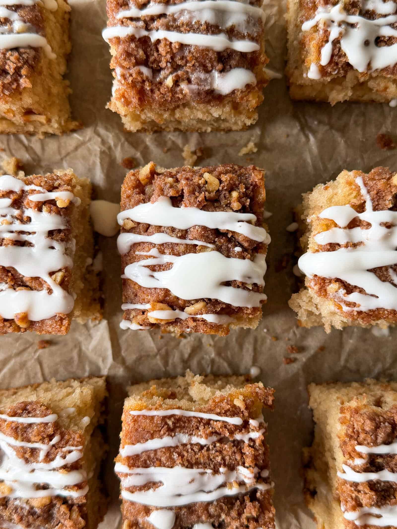 Nine pieces of easy coffee cake with streusel topping and white icing drizzle, arranged on brown parchment paper.