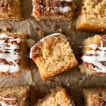Nine square pieces of easy coffee cake with crumb topping and white icing drizzle are arranged on brown parchment paper, with one piece turned to show its moist inside texture—a perfect example of a classic cinnamon coffee cake recipe.