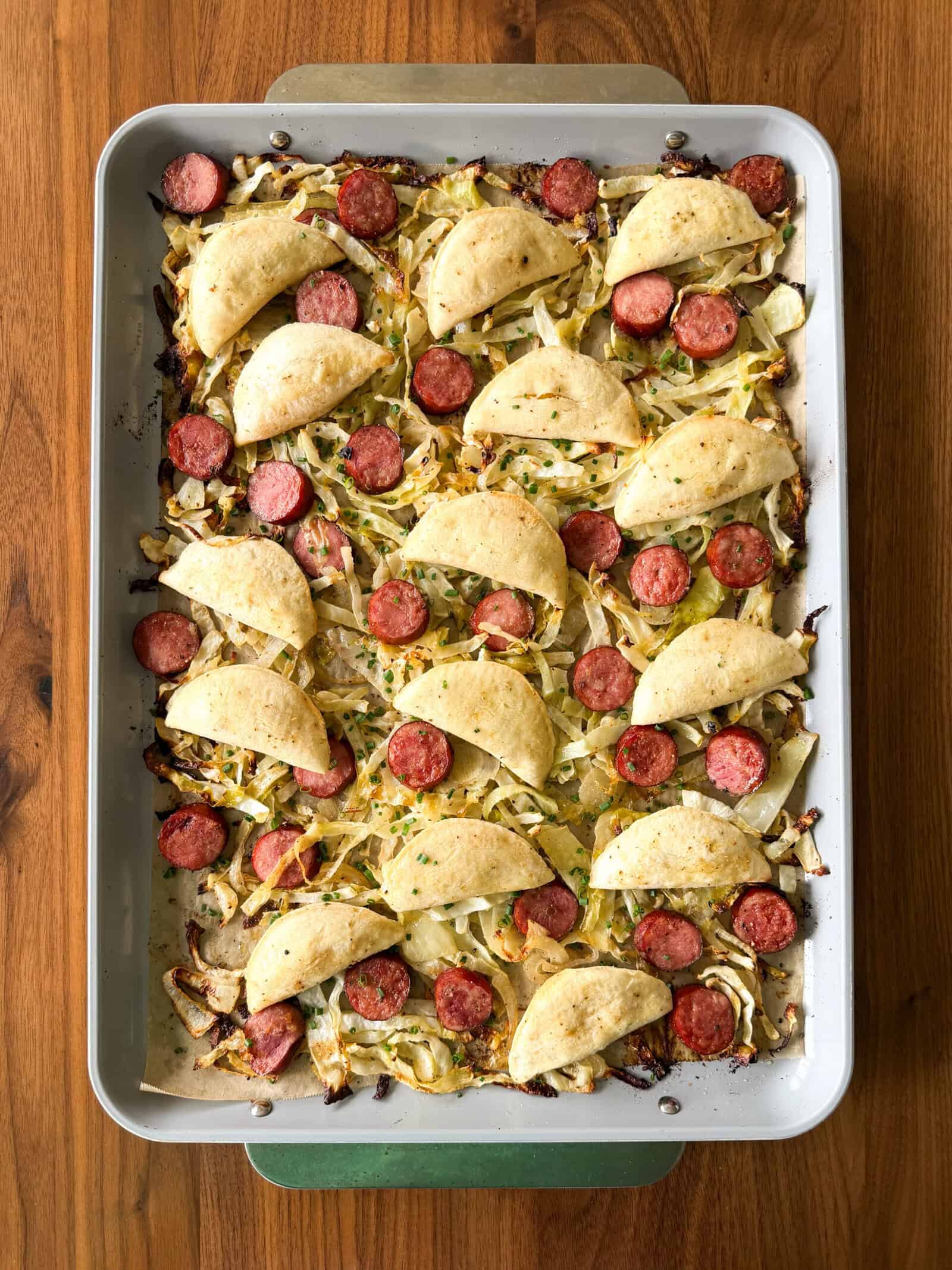 Sheet pan of roasted cabbage, sliced kielbasa, and golden-brown pierogis for an easy pierogi meal.
