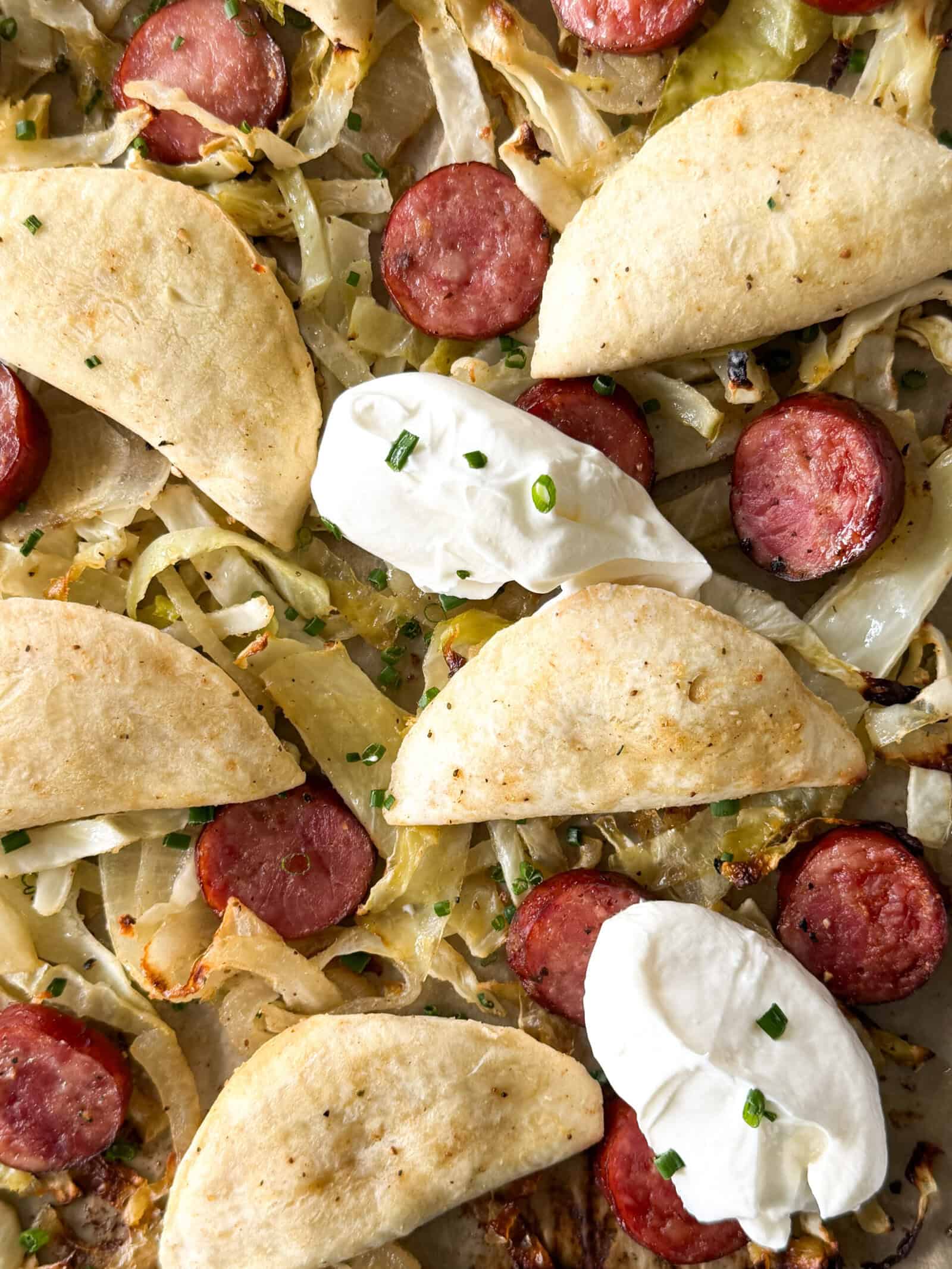 Roasted sheet pan pierogis and kielbasa with cabbage, small folded dumplings, and dollops of sour cream.