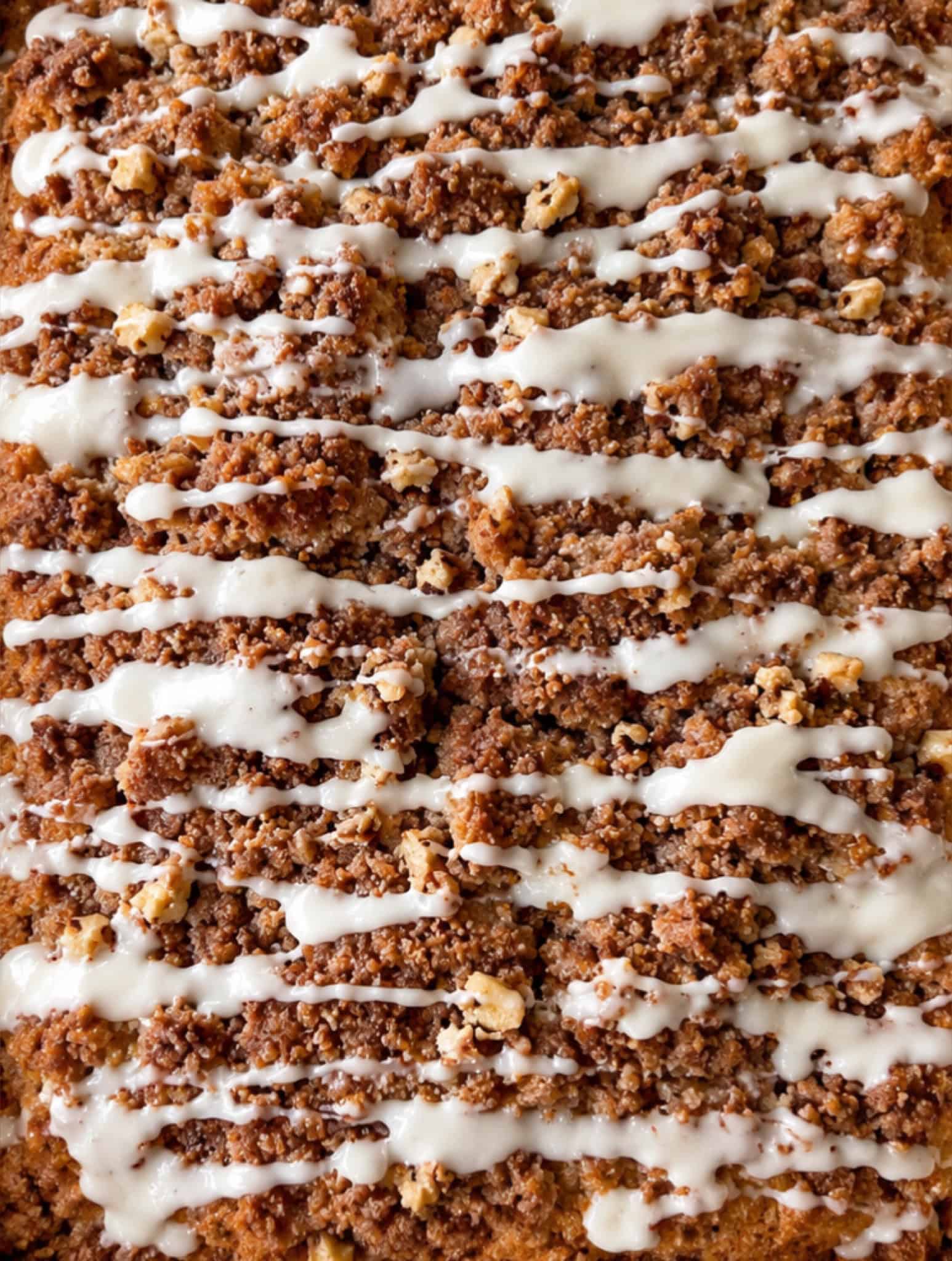 Close-up of a cinnamon coffee cake topped with crumbly brown streusel and drizzled with white icing in diagonal lines, showcasing an easy coffee cake perfect for any occasion.