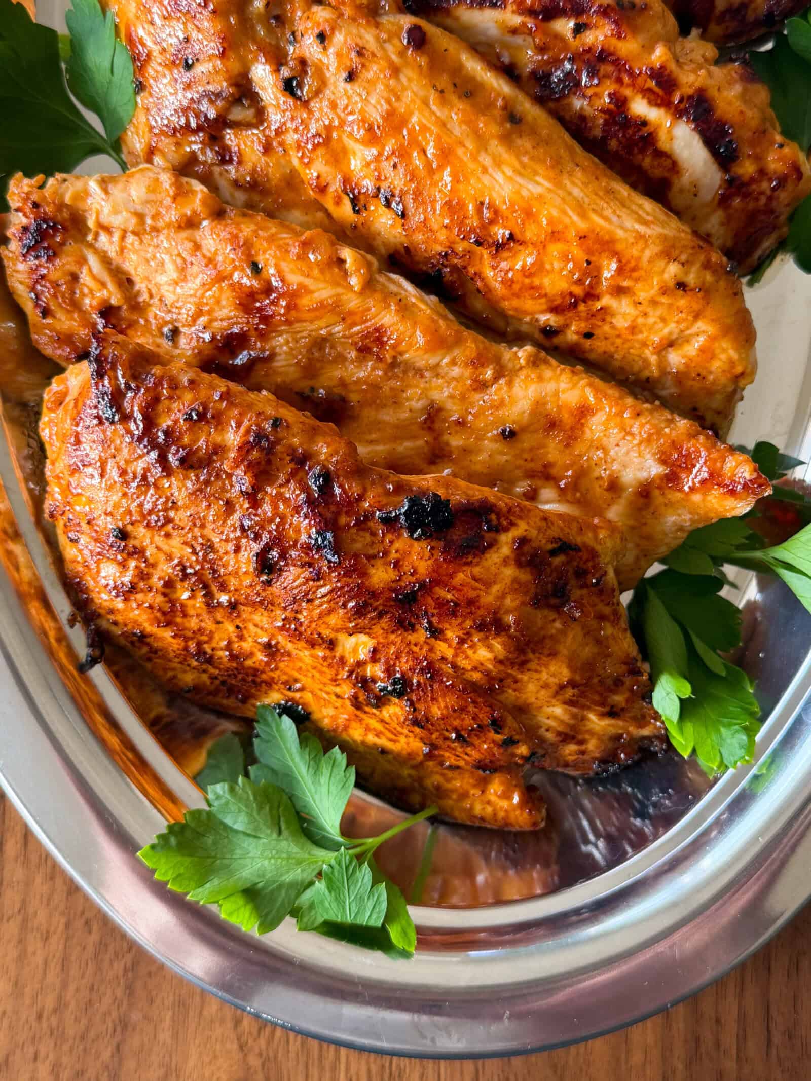 Seared yogurt marinated chicken breast fillets garnished with fresh parsley on a silver platter.