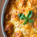 A ravioli with gochujang cream sauce dish baked in a white casserole, topped with melted cheese and fresh basil.