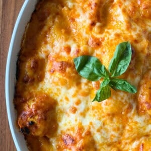 A ravioli with gochujang cream sauce dish baked in a white casserole, topped with melted cheese and fresh basil.