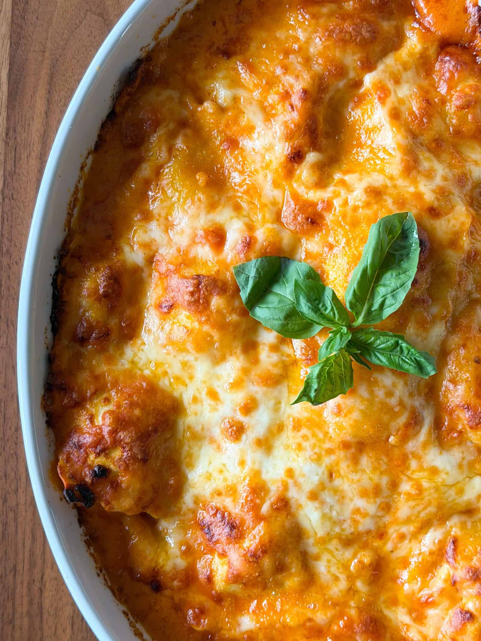 A ravioli with gochujang cream sauce dish baked in a white casserole, topped with melted cheese and fresh basil.