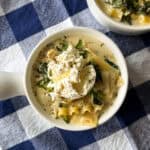 Two bowls of easy lasagna soup topped with dollops of ricotta, herbs, and pepper, resting on a blue and white checkered tablecloth.