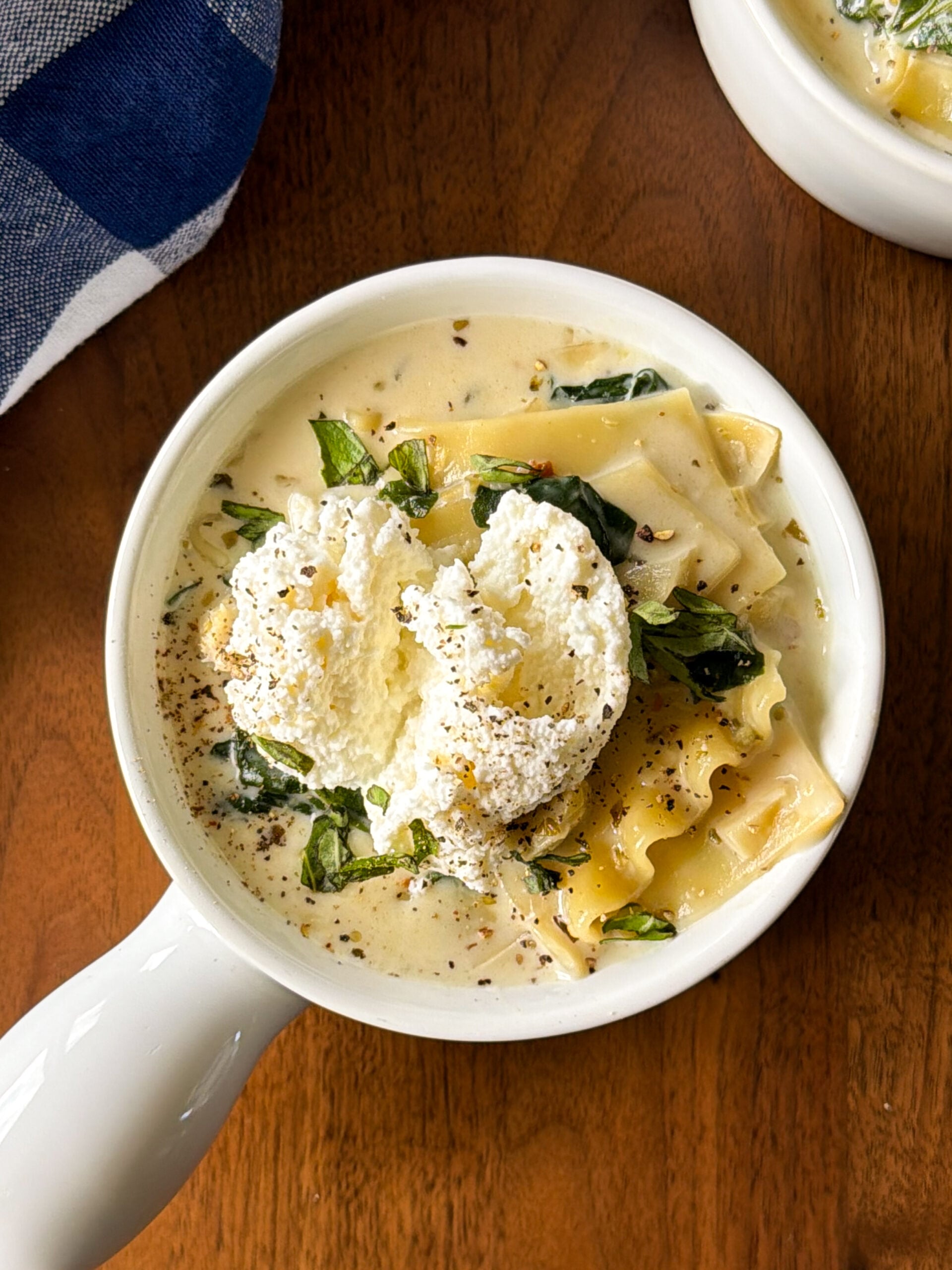 Creamy lasagna soup in a white bowl, topped with a dollop of ricotta cheese, spinach, and cracked black pepper, making for an easy lasagna soup recipe.