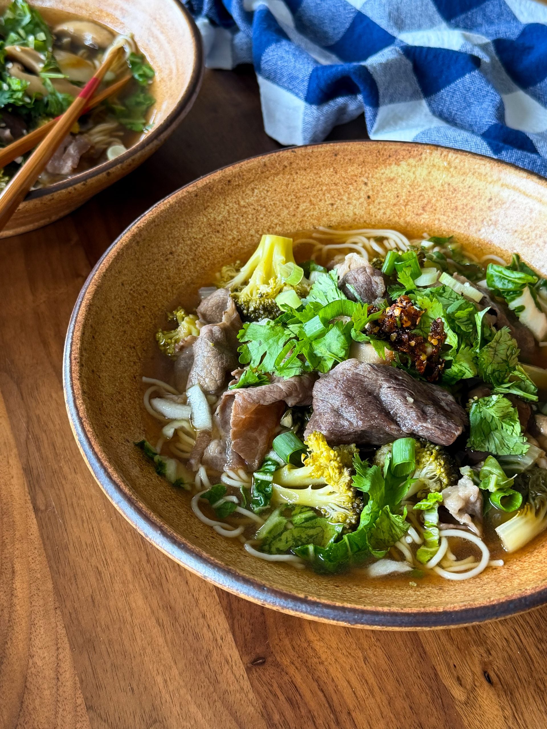 A bowl of Asian inspired beef and noodle soup with broccoli and fresh cilantro, topped with chili oil.
