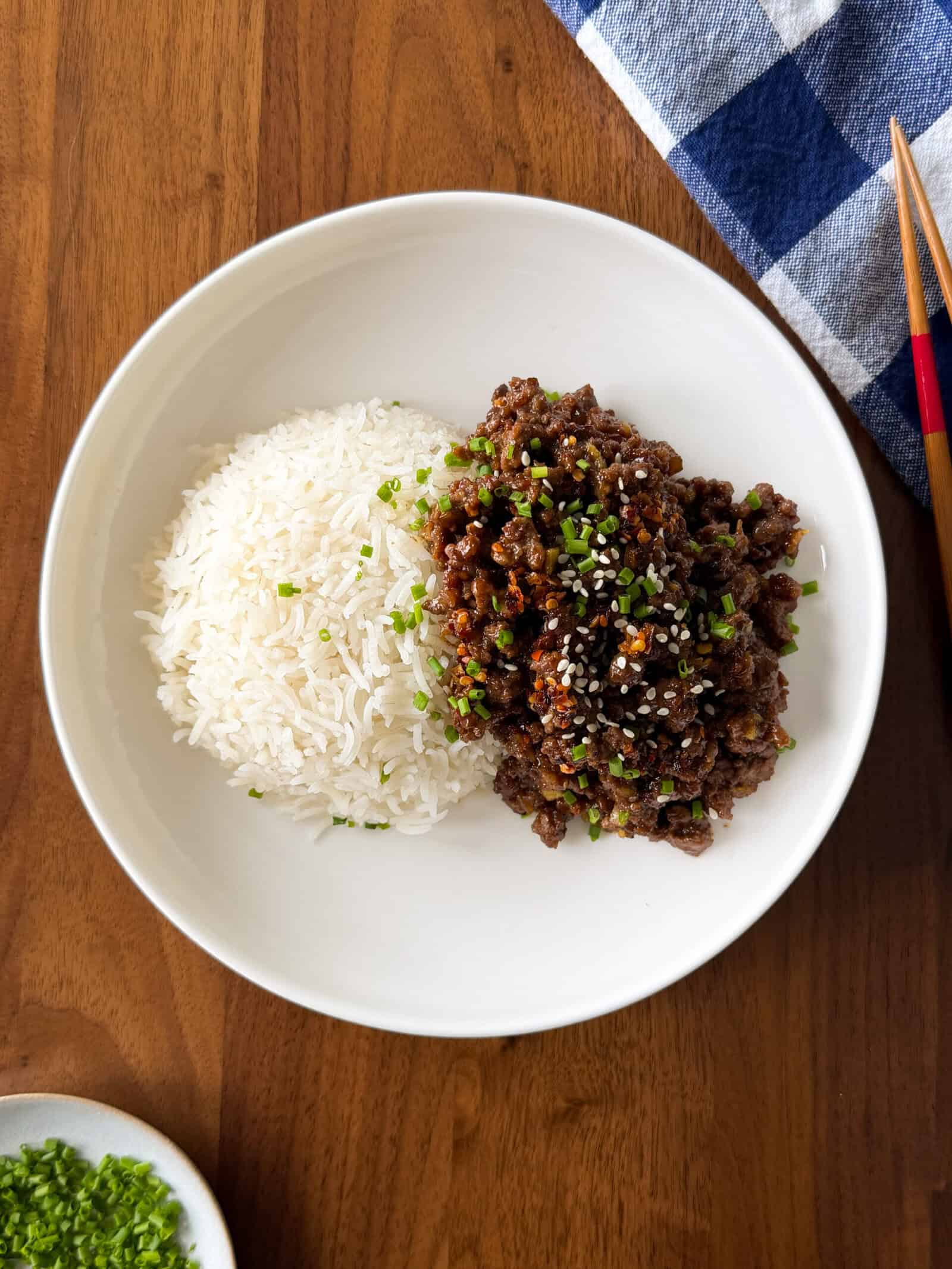 A bowl containing a mound of white rice next to a portion of sticky honey ginger ground beef topped with sesame seeds and chopped green onions.