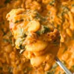 A spoonful of Marry Me Butter Beans in a creamy tomato sauce with spinach, held over a serving dish.