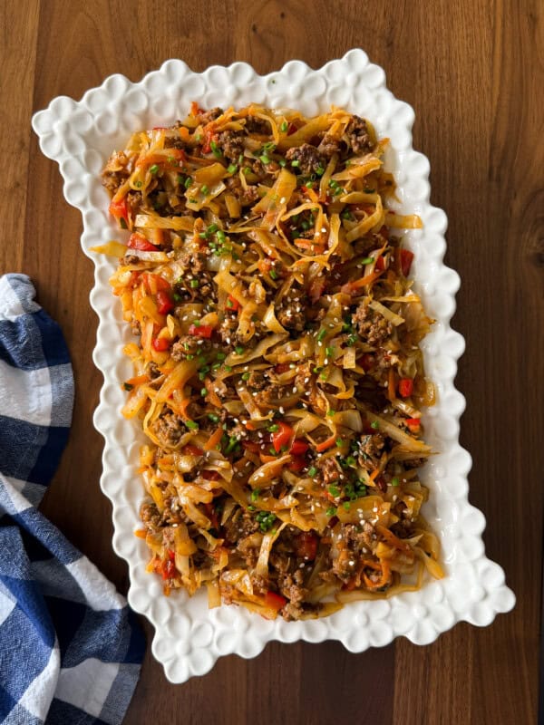 A rectangular serving platter piled with a dirty cabbage stir-fry made of ground meat, shredded cabbage, and red peppers, topped with sesame seeds and green onions.
