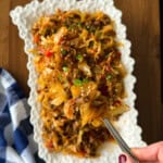 A serving spoon lifts a portion of dirty cabbage from a white decorative platter, revealing a mixture of sautéed cabbage, ground meat, and peppers.