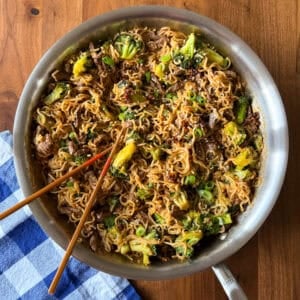 A skillet filled with beef and broccoli ramen, with wooden chopsticks resting inside.