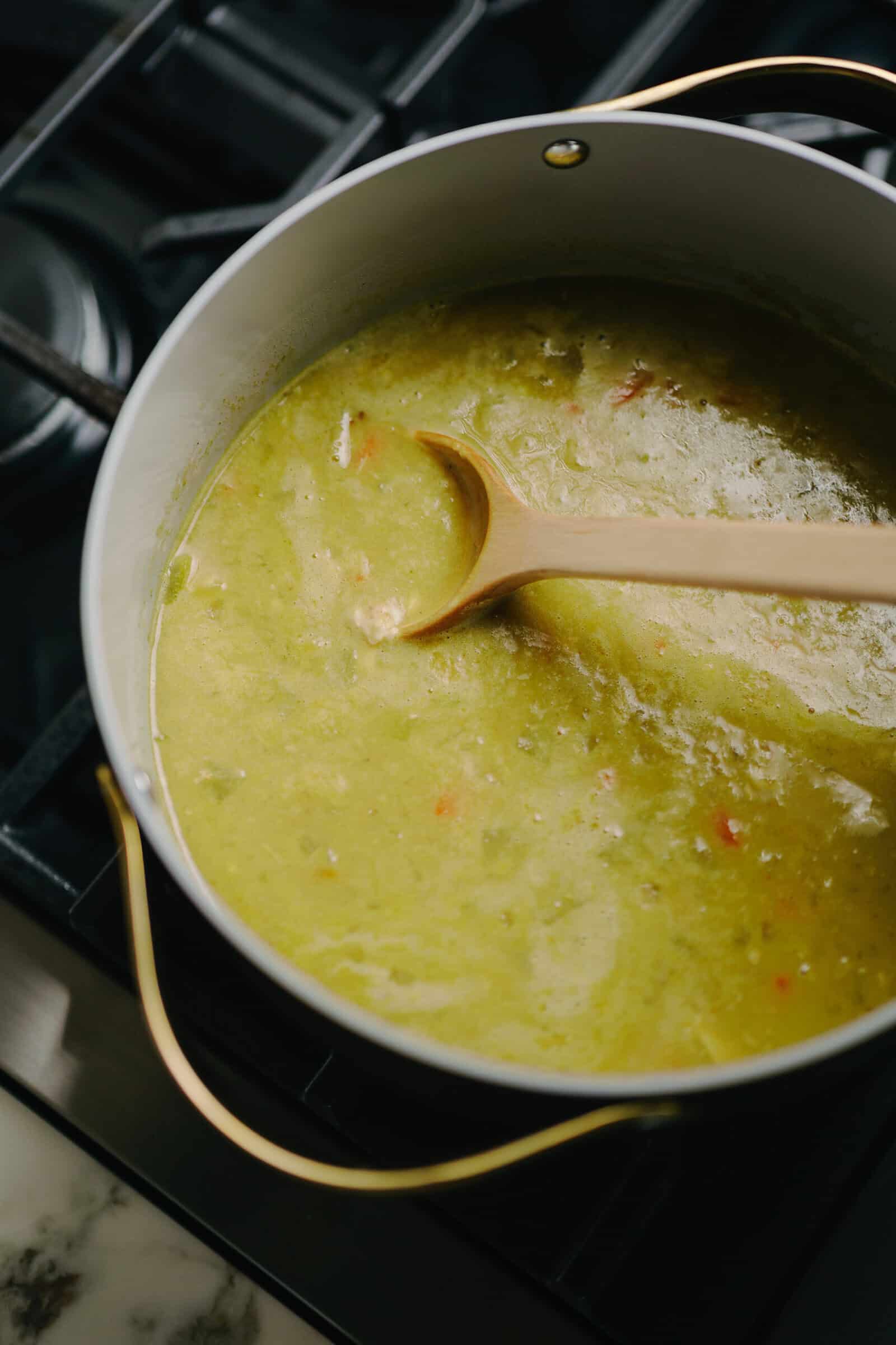 A wooden spoon rests in a pot of thick green vegetable soup on a stovetop.